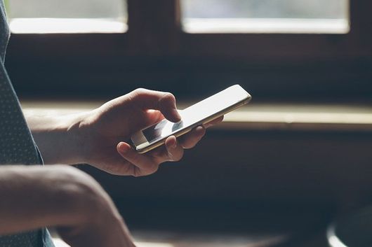 La mano de una persona usando un smartphone, tocando la pantalla con un dedo. El teléfono es dorado.