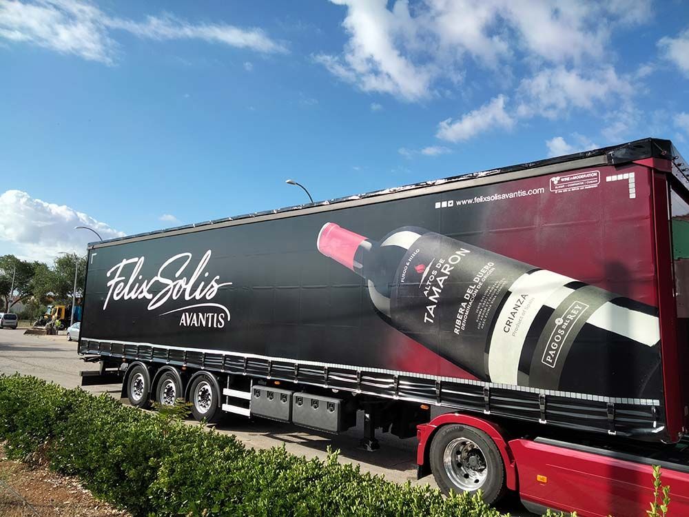 Camión con un gran anuncio de botellas de vino de Félix Solís. Colores oscuros, estacionado afuera bajo un cielo azul.