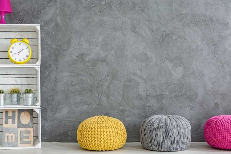 Estanterías blancas con decoración, reloj amarillo, pared gris y pufs de colores.