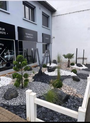 Un jardin de gravier moderne et minimaliste devant un bâtiment gris avec une enseigne noire en façade.