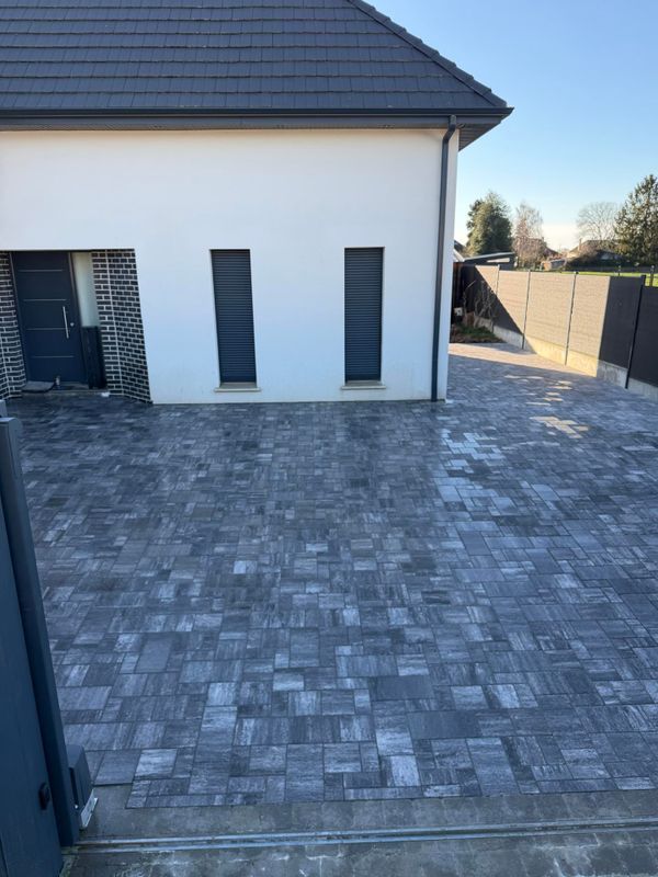Une maison blanche avec deux fenêtres verticales au-dessus d'une allée en pierre grise à motifs menant à une porte d'entrée sombre.