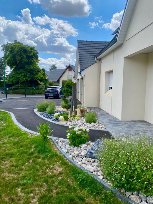Maison de banlieue avec parterres de gravier, pelouse verte et voiture garée sous un ciel d'un bleu éclatant