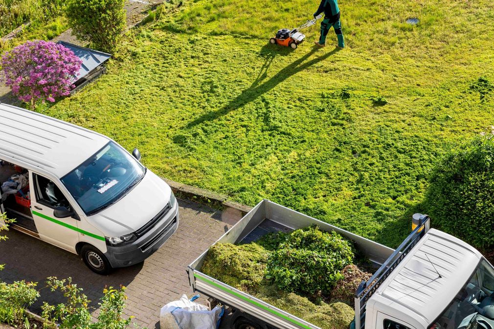 Ein Mann mäht das Gras neben einem mit Gras beladenen Lastwagen.