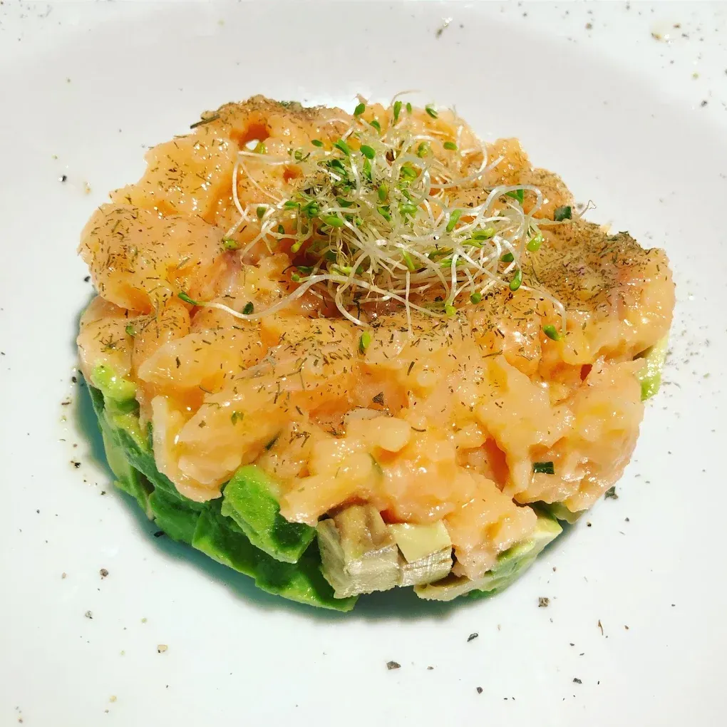Tartar de salmón con aguacate y brotes en plato blanco, espolvoreado con pimienta negra.
