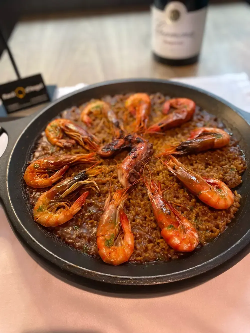 Paella con camarones a la plancha en sartén negra, servida en mesa.