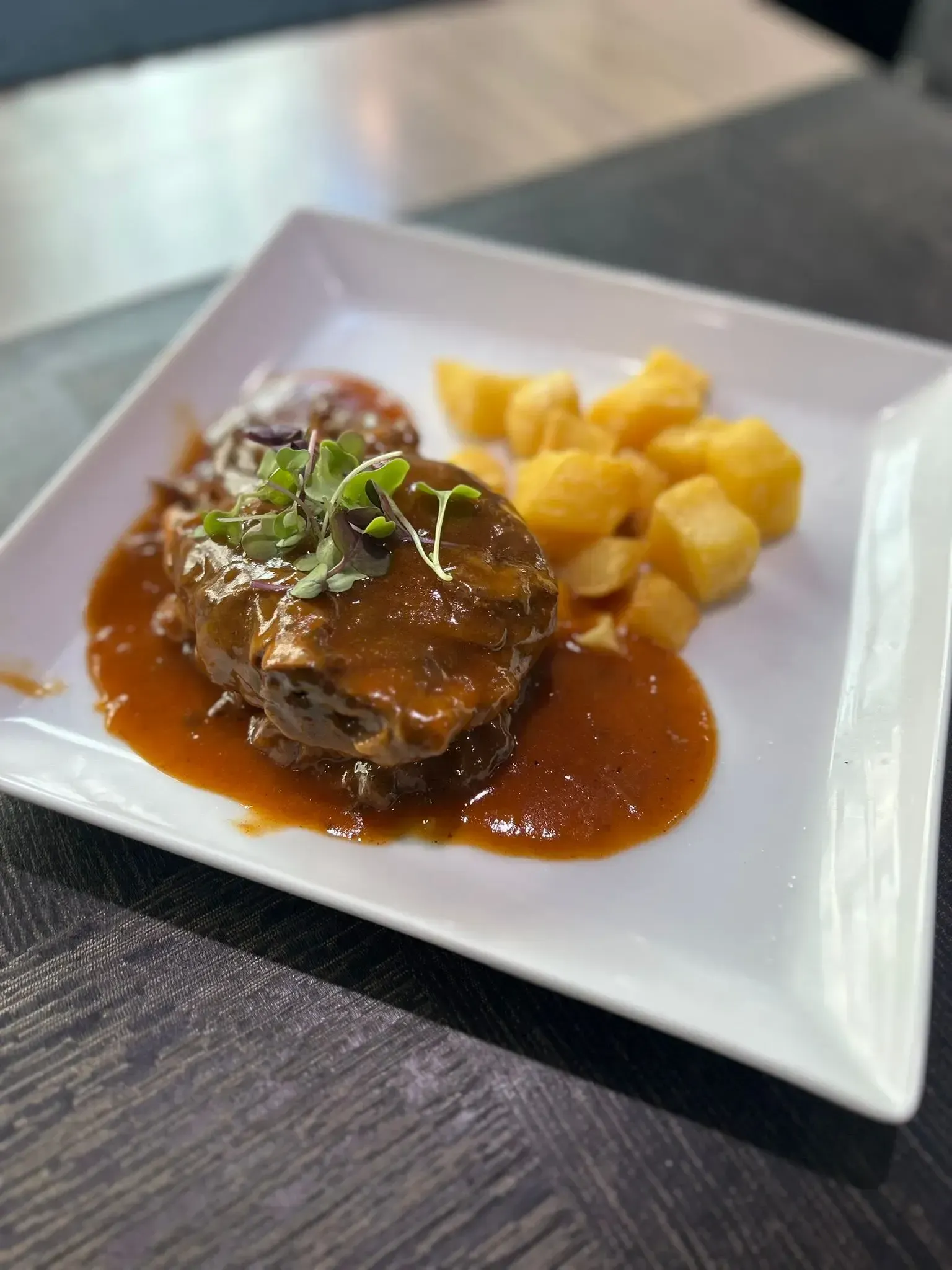 Plato de ternera con salsa, patatas asadas y verduras en un plato blanco.