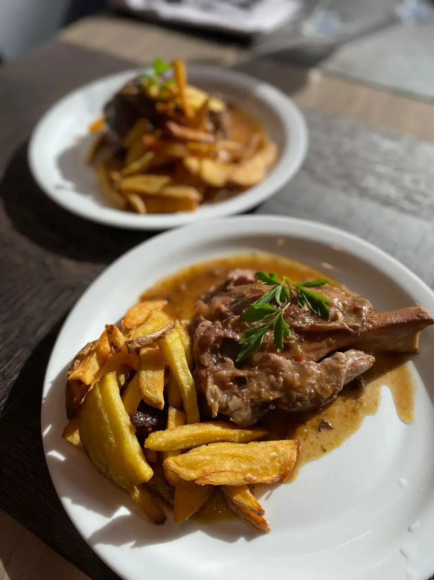 Dos platos de comida: uno con carne, patatas fritas y salsa; el otro similar, pero difuminado.