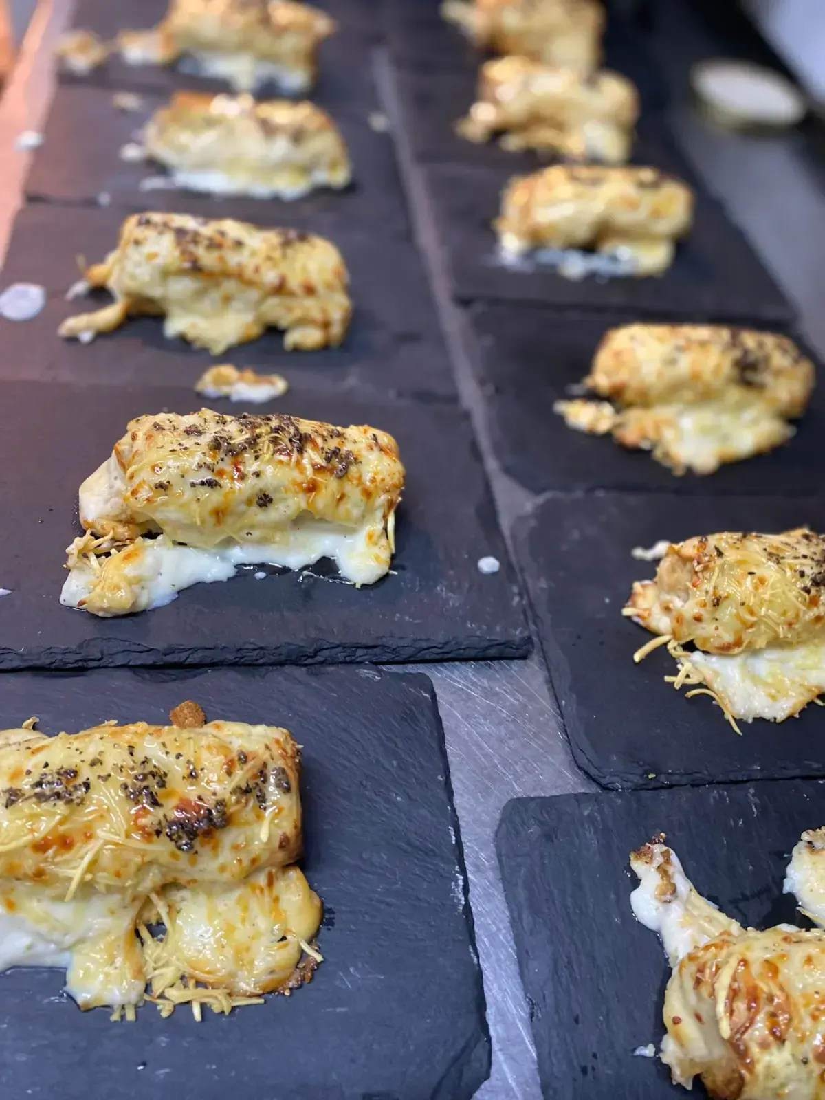 Porciones de aperitivo de pescado al horno en bandejas de pizarra negra.