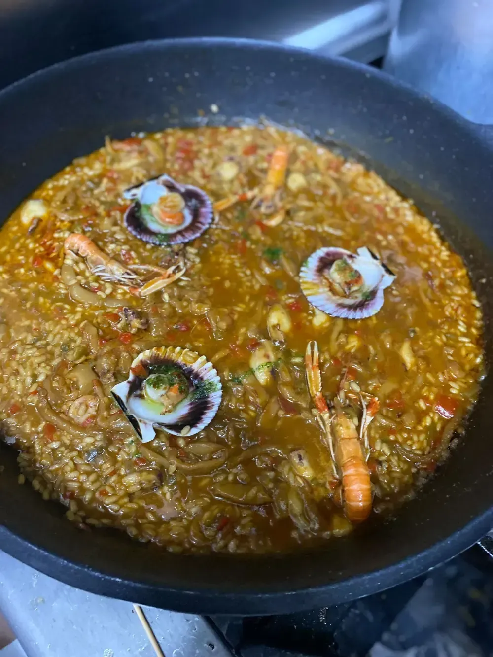 Paella de mariscos en sartén, con mariscos y camarones. Caldo de color naranja-marrón, cocinado.