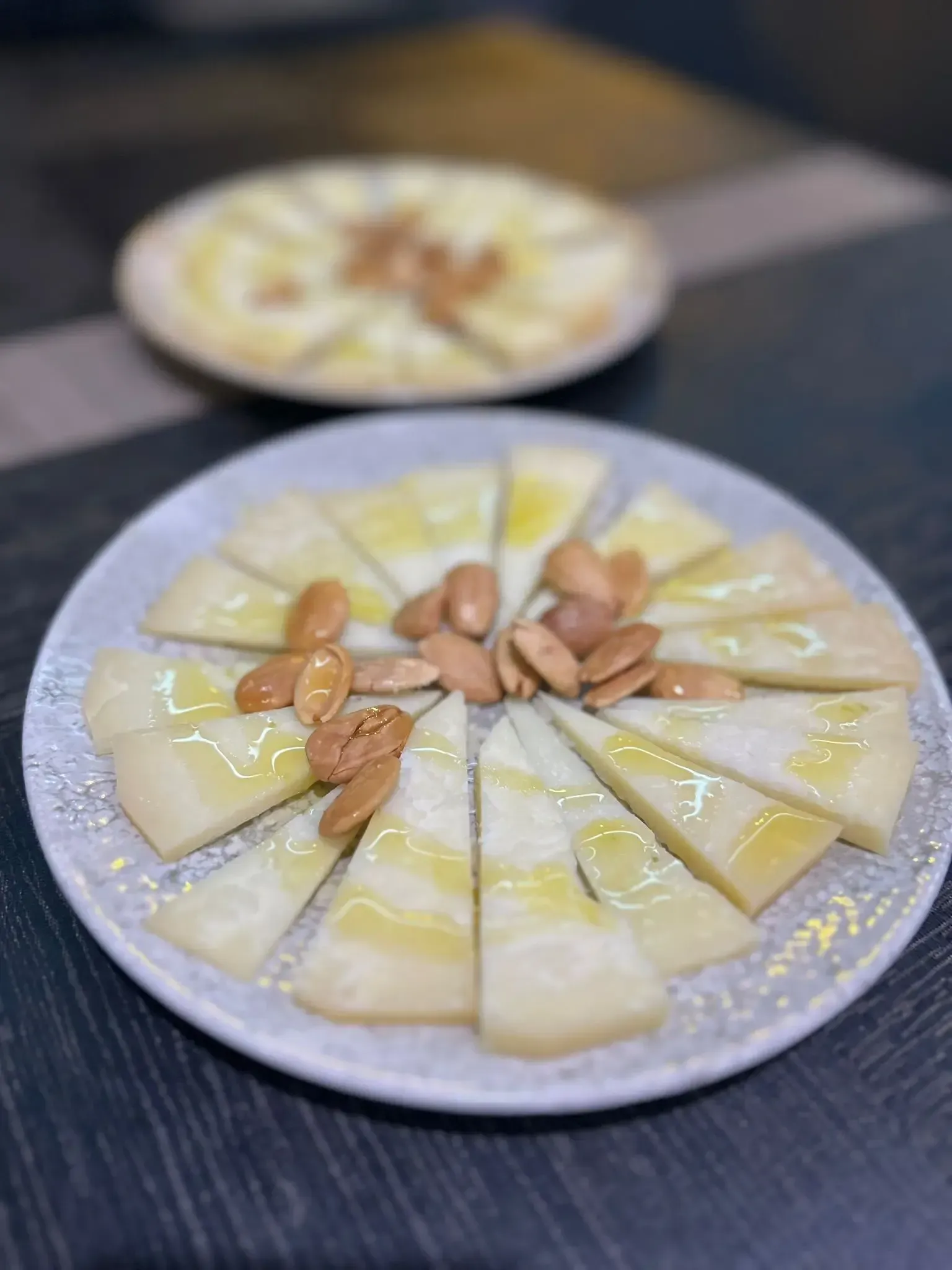 Platos de lonchas de queso rociados con aceite y cubiertos con almendras. Mesa oscura.