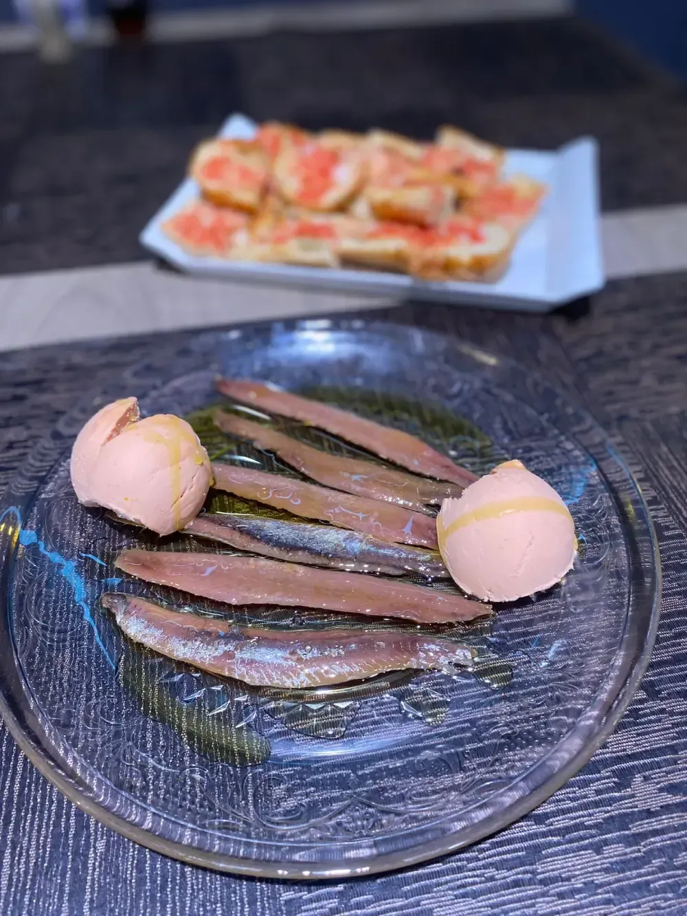 Anchoas en plato de cristal con ajo y bandeja de pan con tomate.