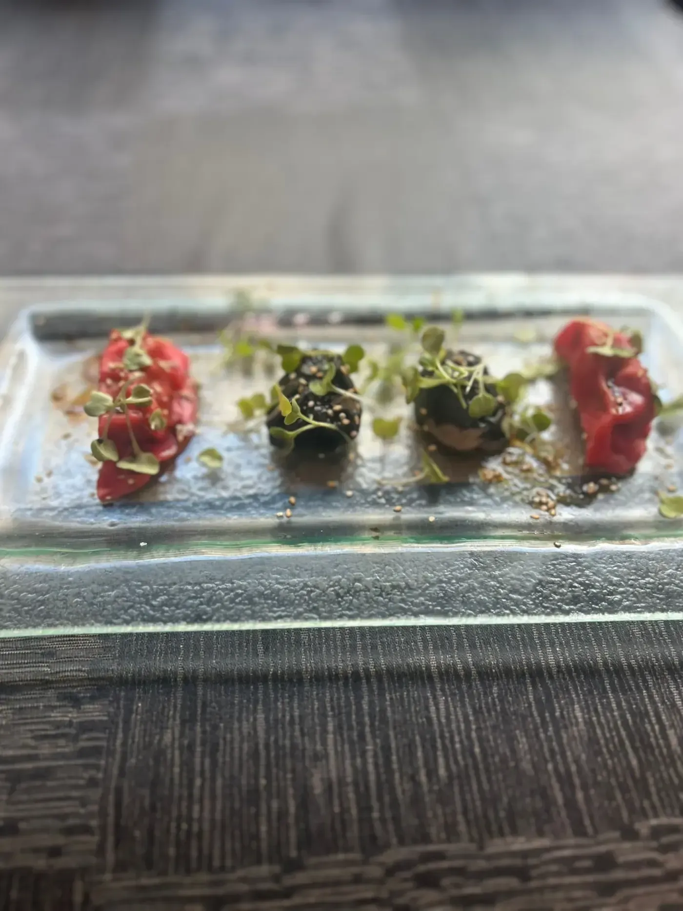 Cuatro pequeños alimentos en un plato de vidrio rectangular, adornados