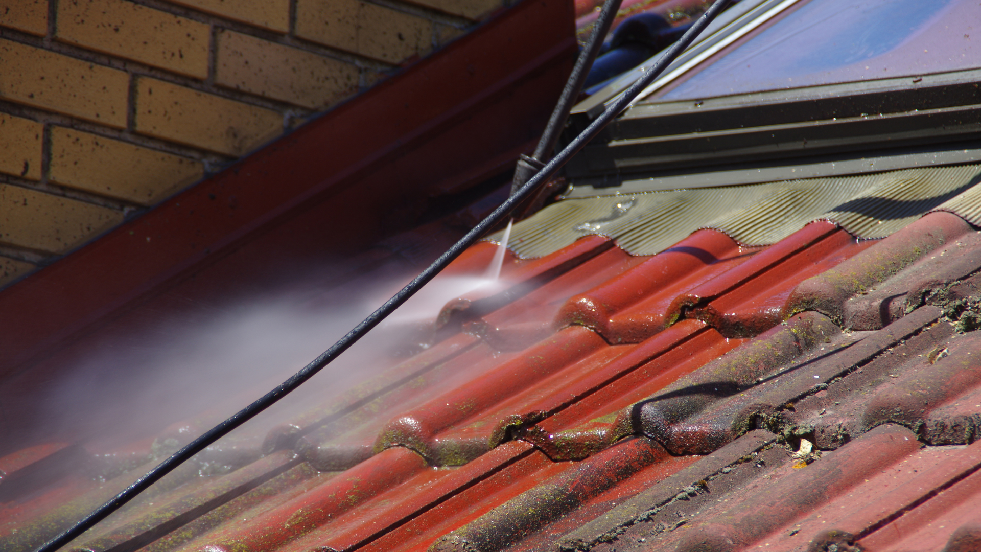 Nettoyage à haute pression d'un toit de tuiles rouges ; jets d'eau, mur de briques en arrière-plan.