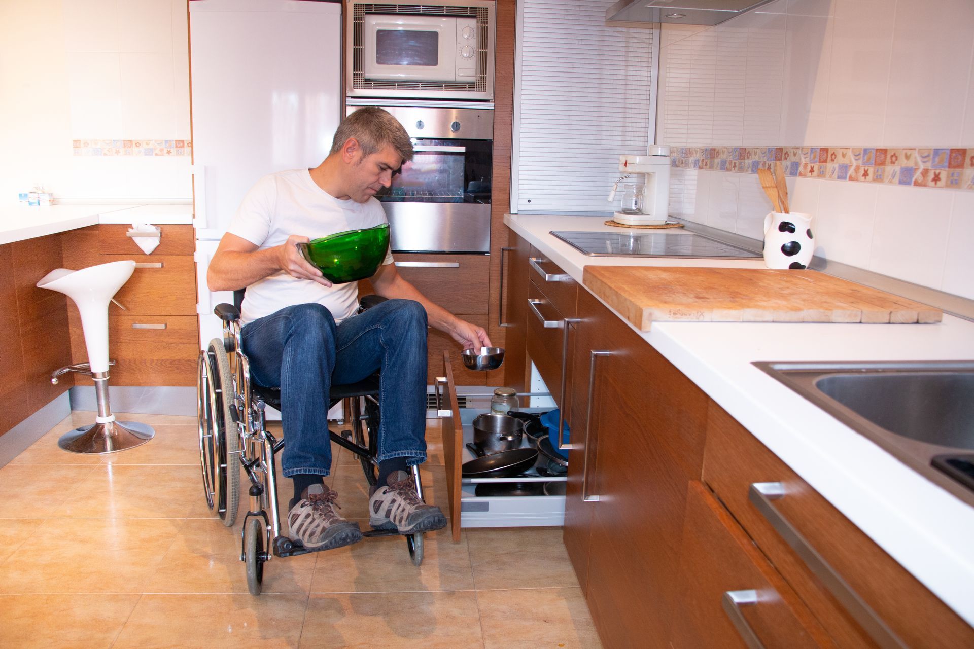 Une personne en fauteuil roulant prépare des repas dans une cuisine moderne avec un bol vert.