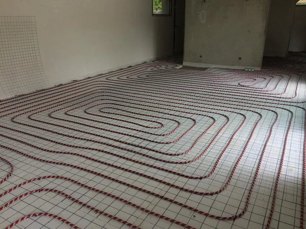 Plombier-chauffagiste qui pose des lames de plancher sur les conduits chauffants