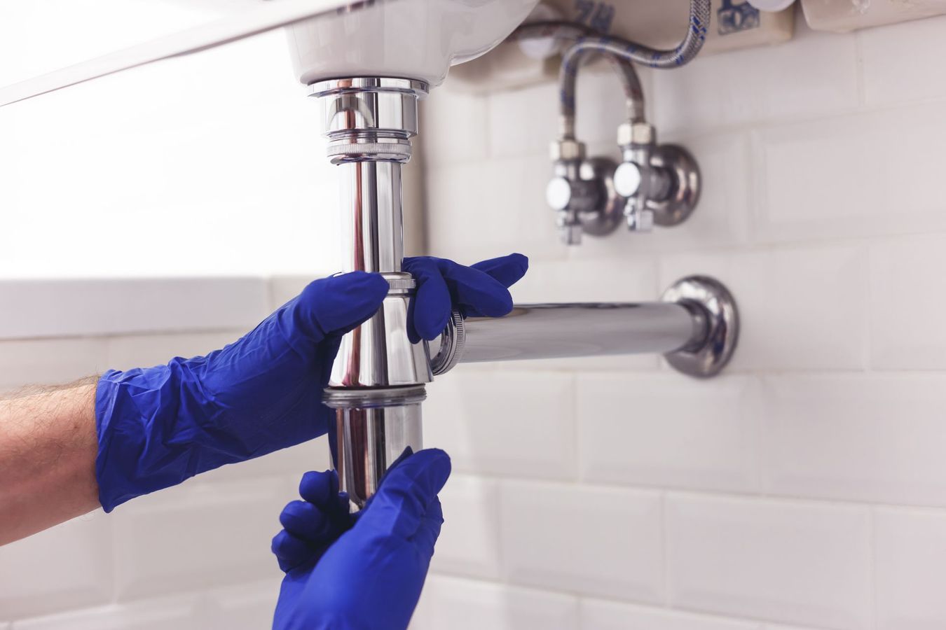 Deux mains dans des gants bleus qui resserrent un siphon d'évier