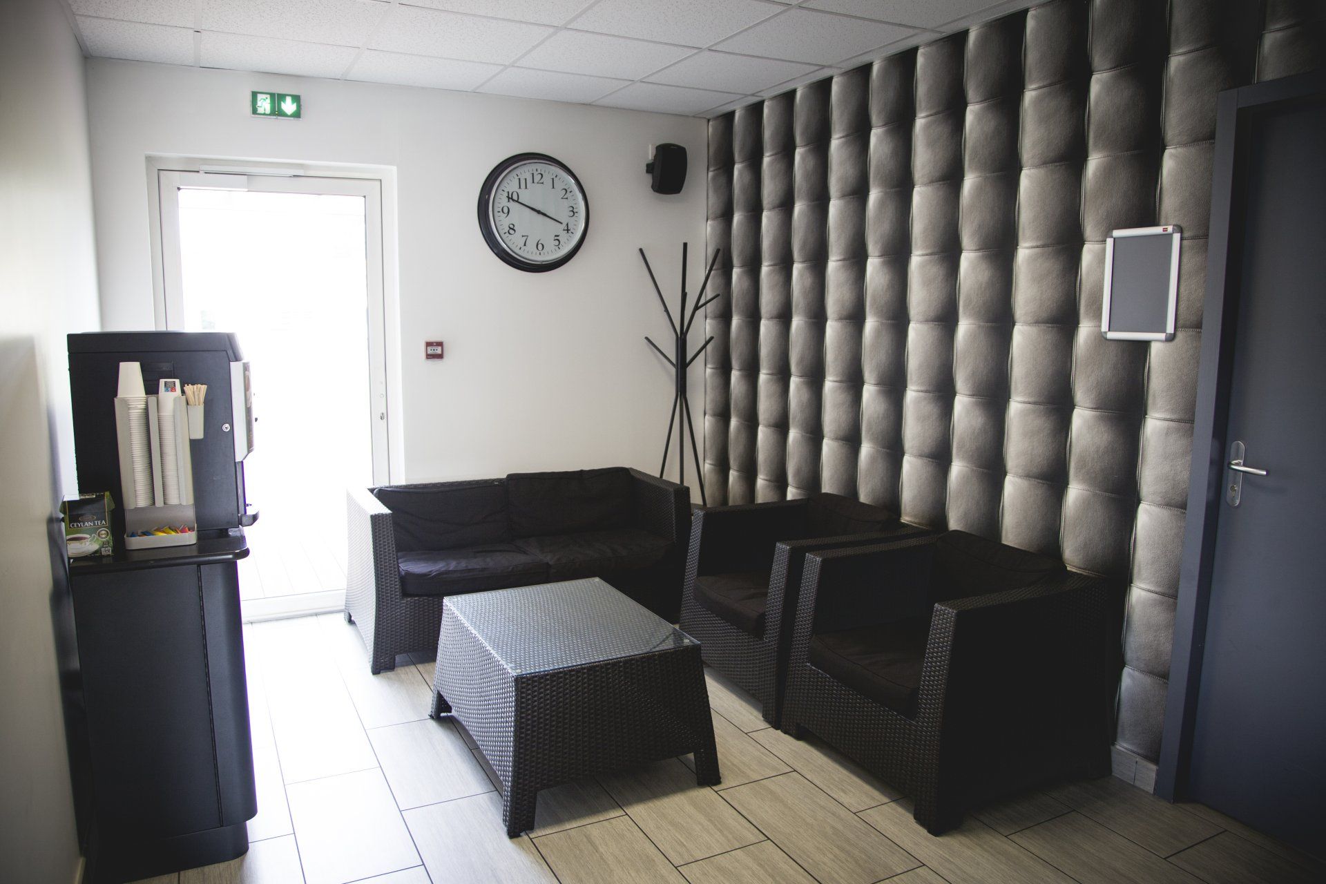Coin salon avec mobilier noir, mur texturé, horloge et porte ouverte.