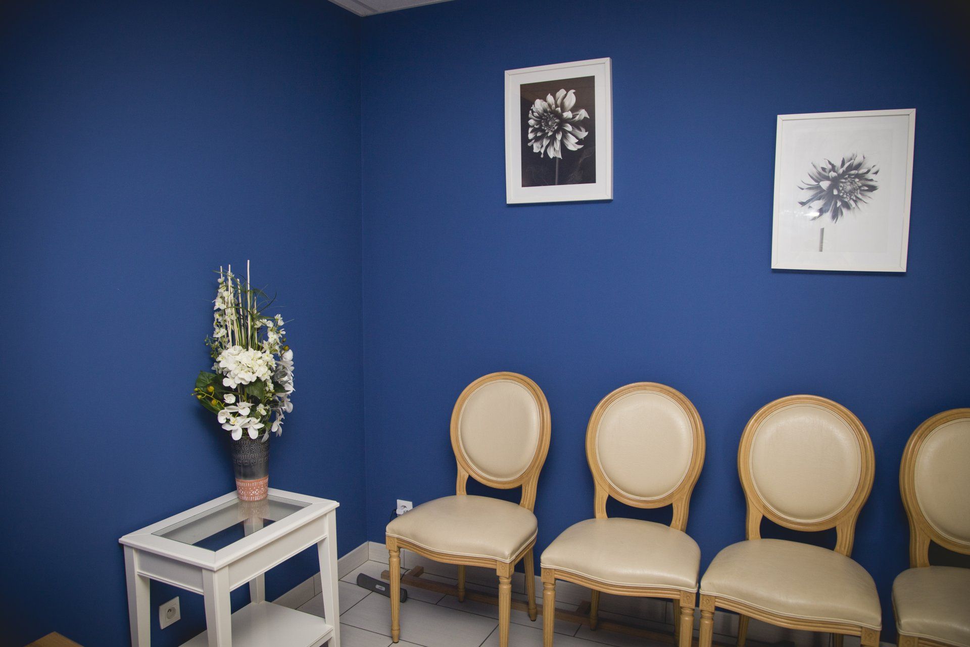 Salle d'attente bleue avec chaises, œuvres d'art et fleurs.