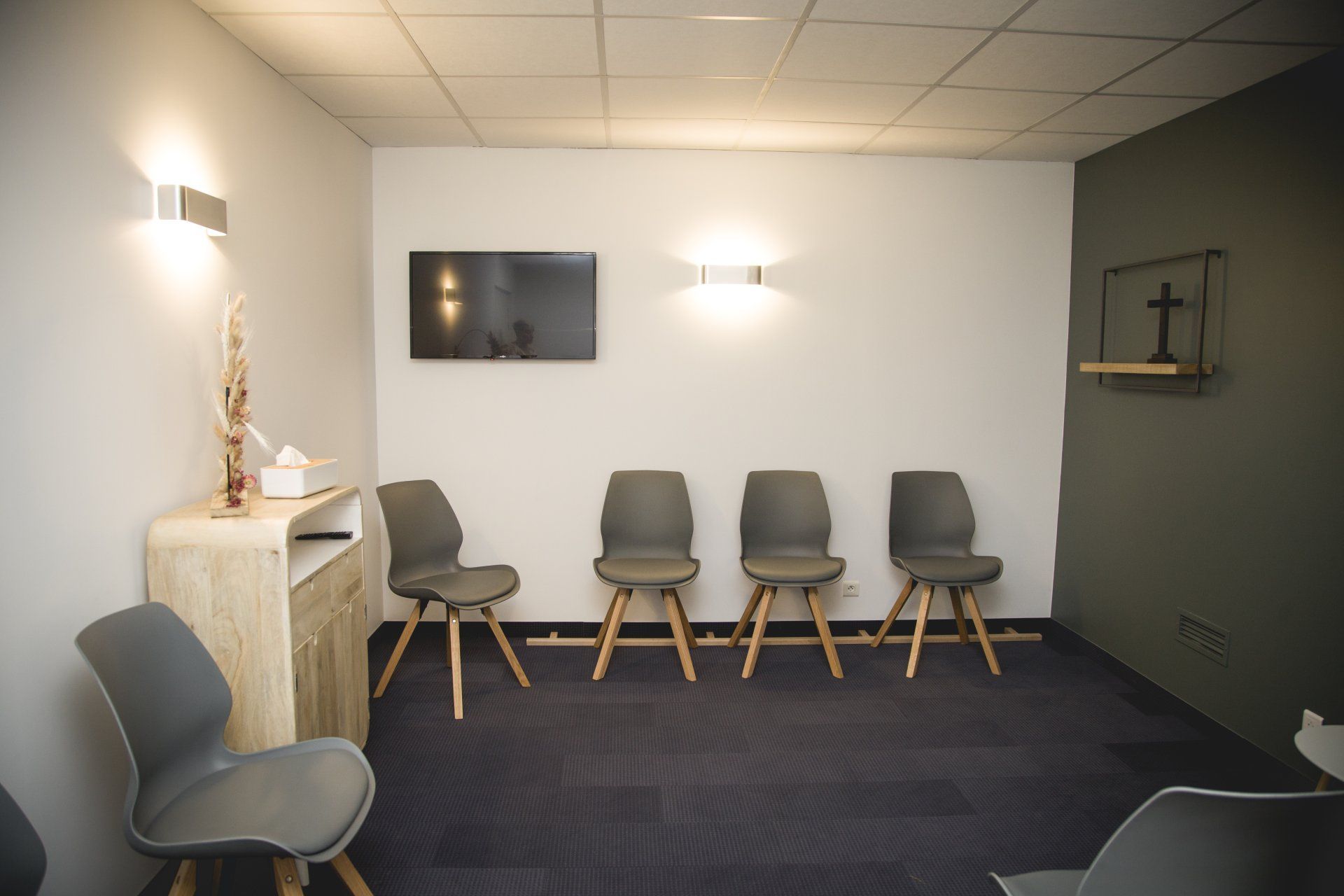 Salle d'attente avec chaises, télévision et appliques murales. Moquette bleu foncé.