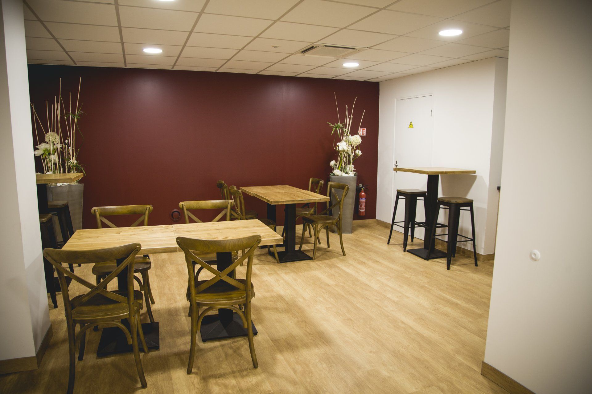 Salle à manger du restaurant avec tables et chaises en bois, mur d'accent rouge et parquet clair.
