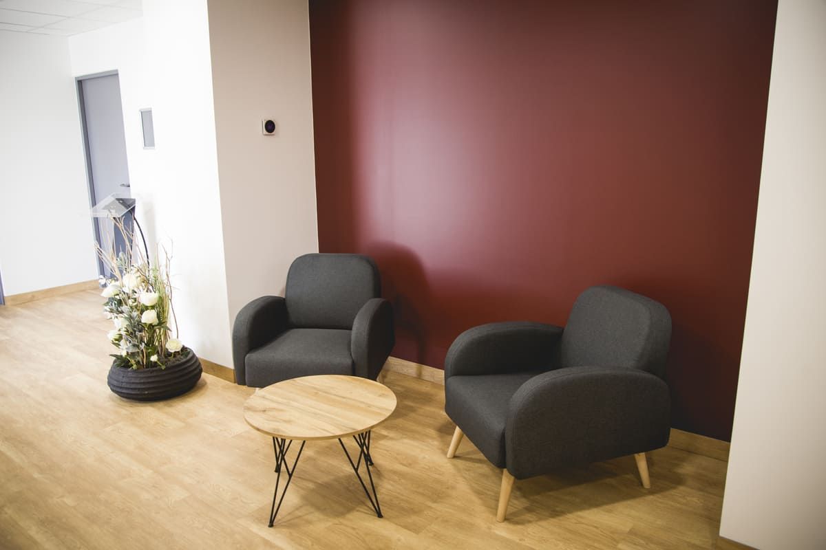 Deux fauteuils gris foncé et une petite table ronde devant un mur bordeaux.