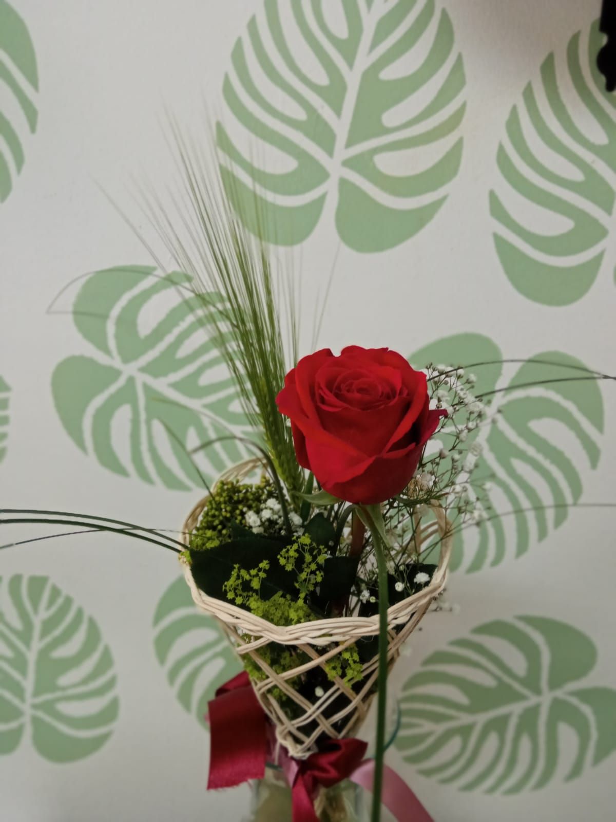 Una rosa roja en una canasta de mimbre con hojas en el fondo.