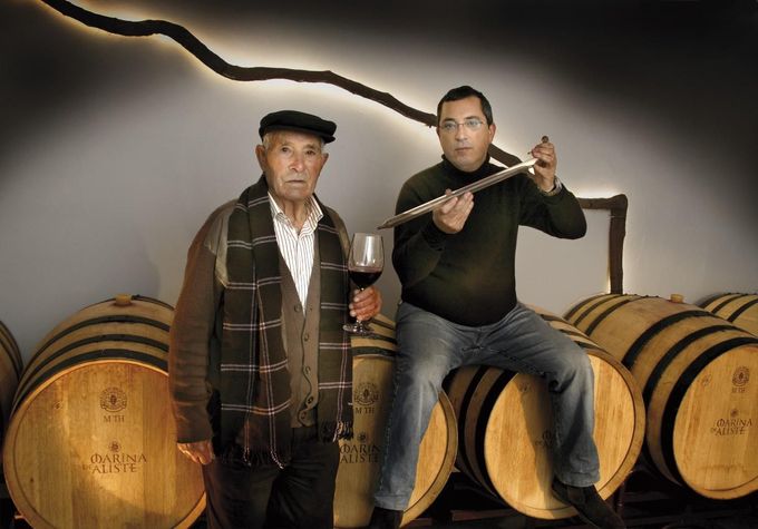 Dos hombres en una bodega, uno sosteniendo una copa de vino