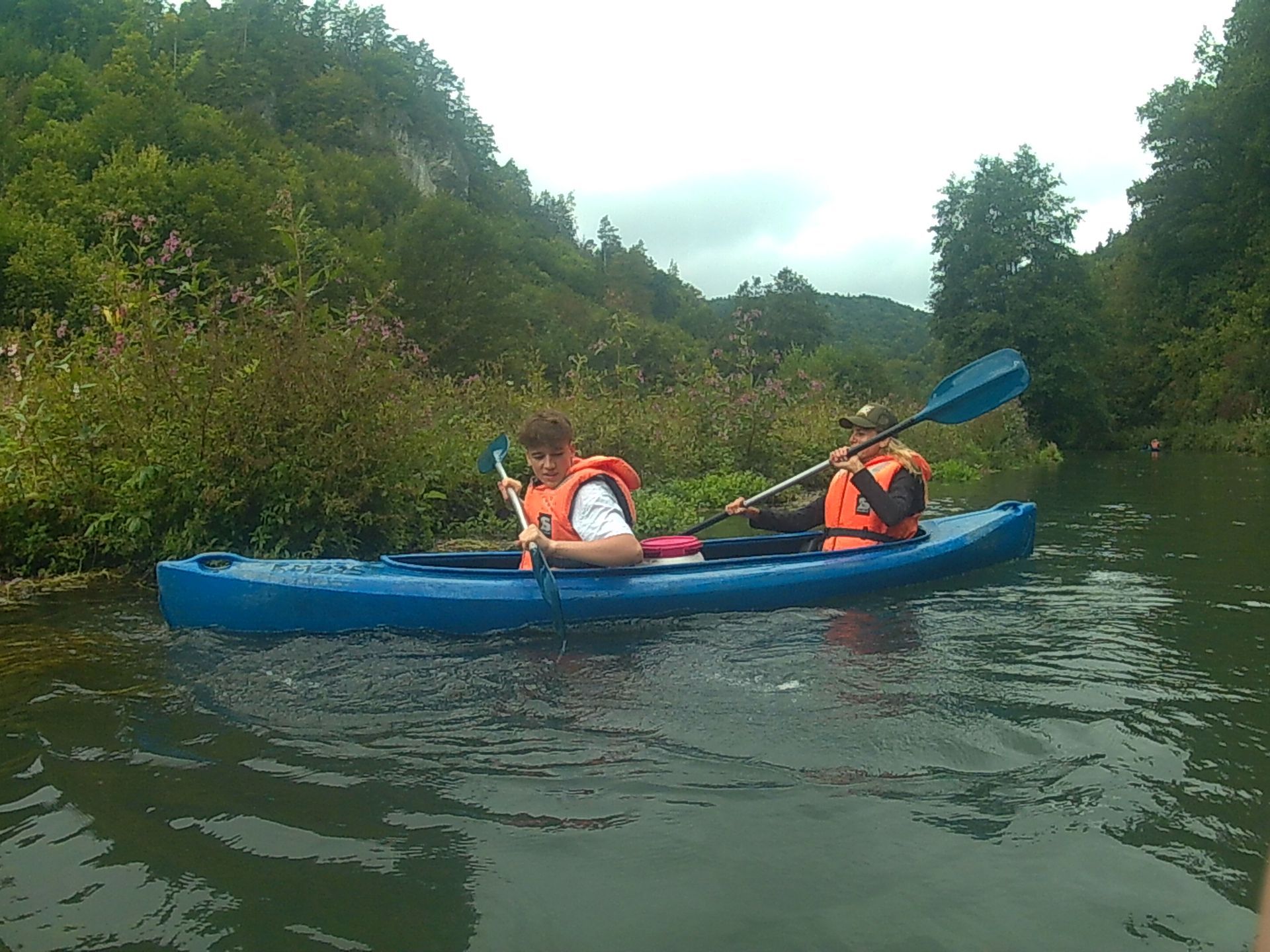 Zwei Personen sind in einem blauen Kajak auf einem Fluss.