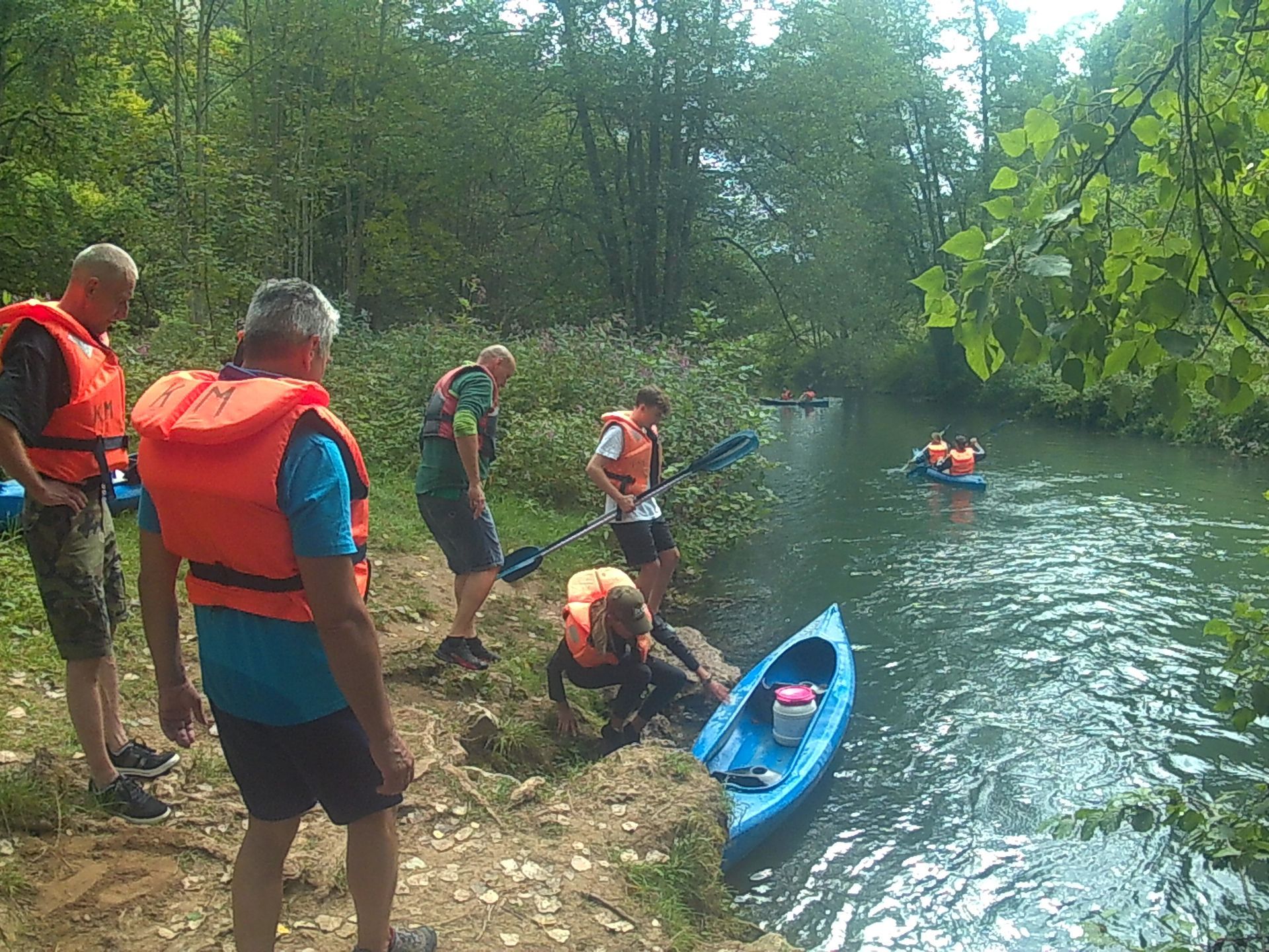 Eine Gruppe von Menschen steht am Ufer eines Flusses in der Nähe eines Kajaks.