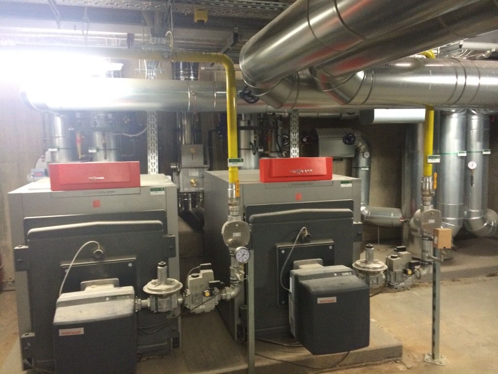 In einem Raum mit Rohren stehen zwei Heizkessel nebeneinander.