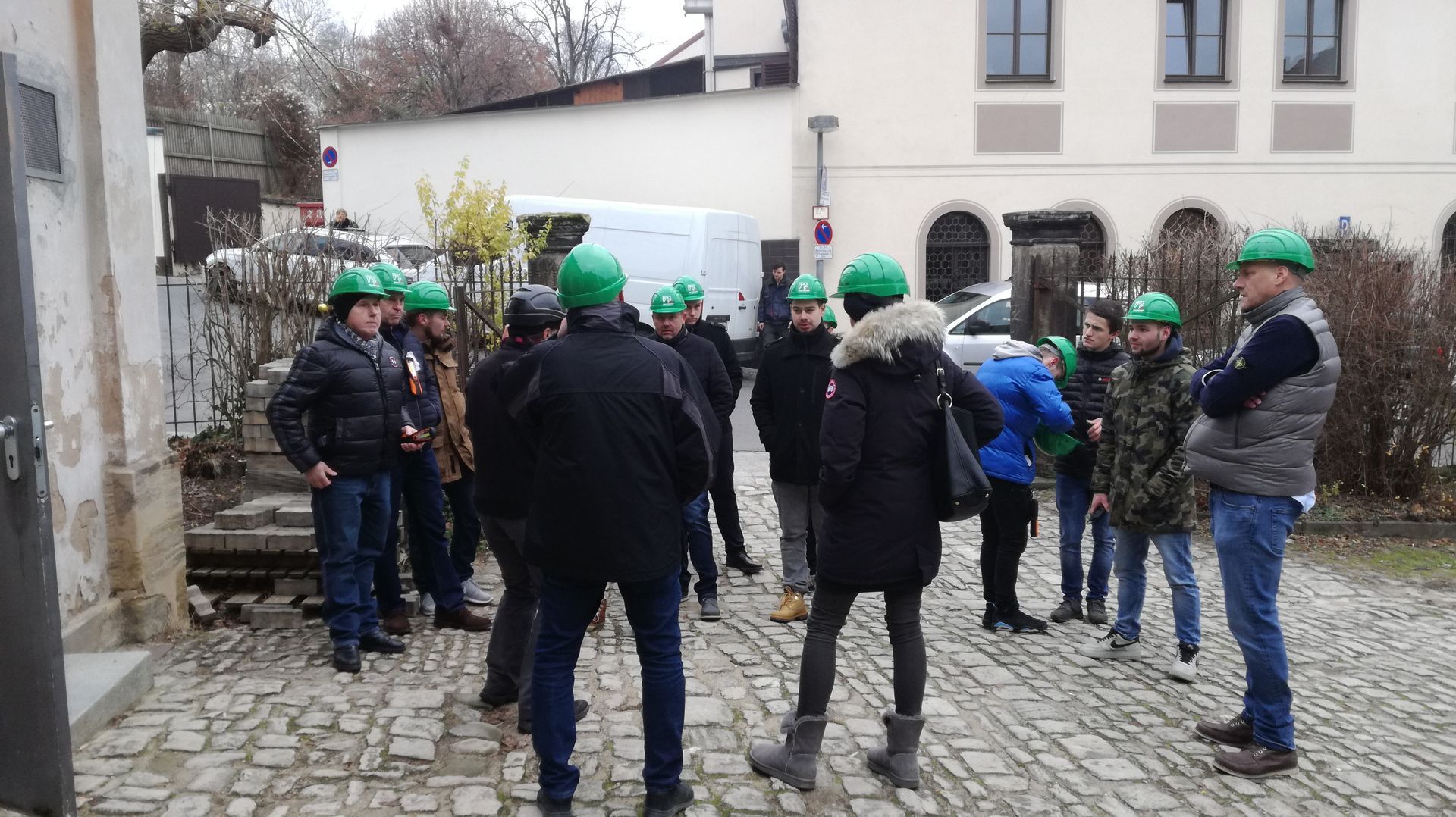 Eine Gruppe von Menschen mit Schutzhelmen steht auf einer Kopfsteinpflasterstraße.