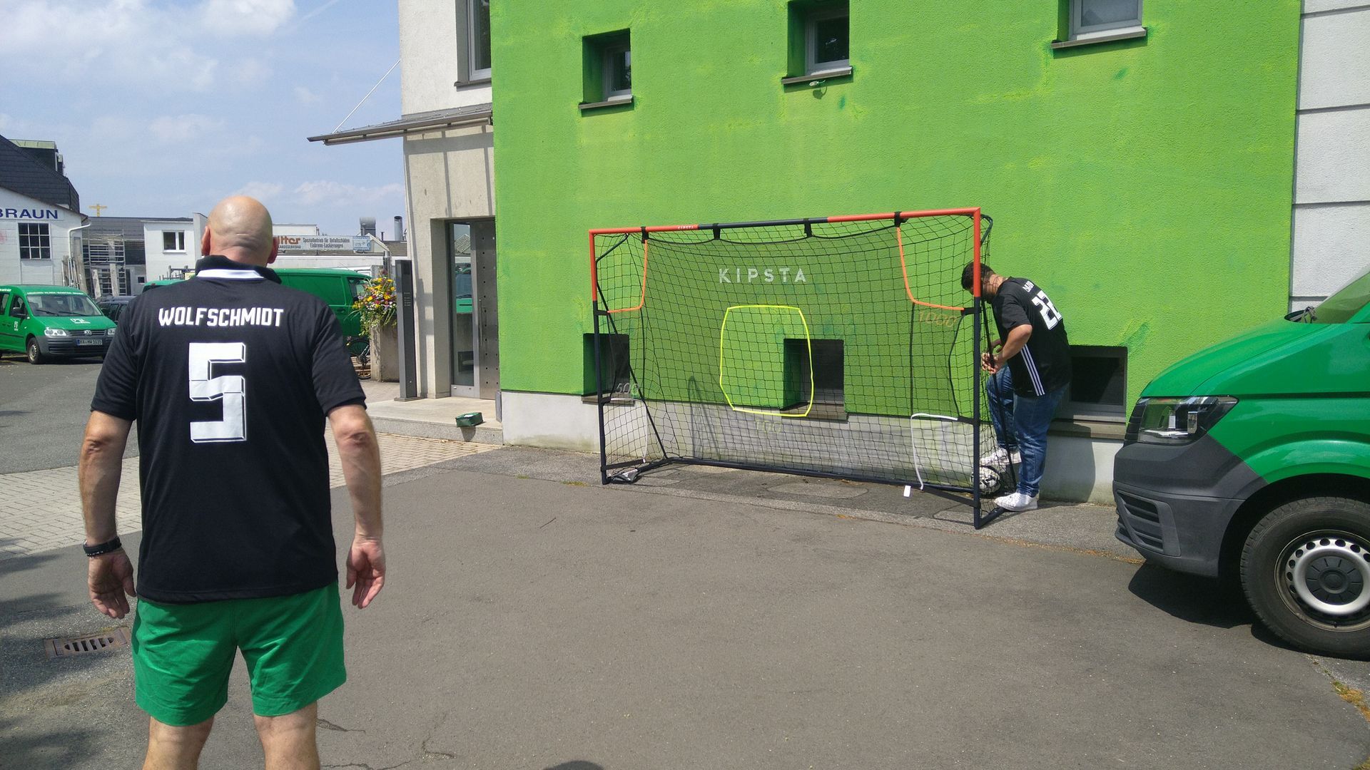 Ein Mann in einem schwarzen Hemd mit der Nummer 5 steht vor einem grünen Gebäude.