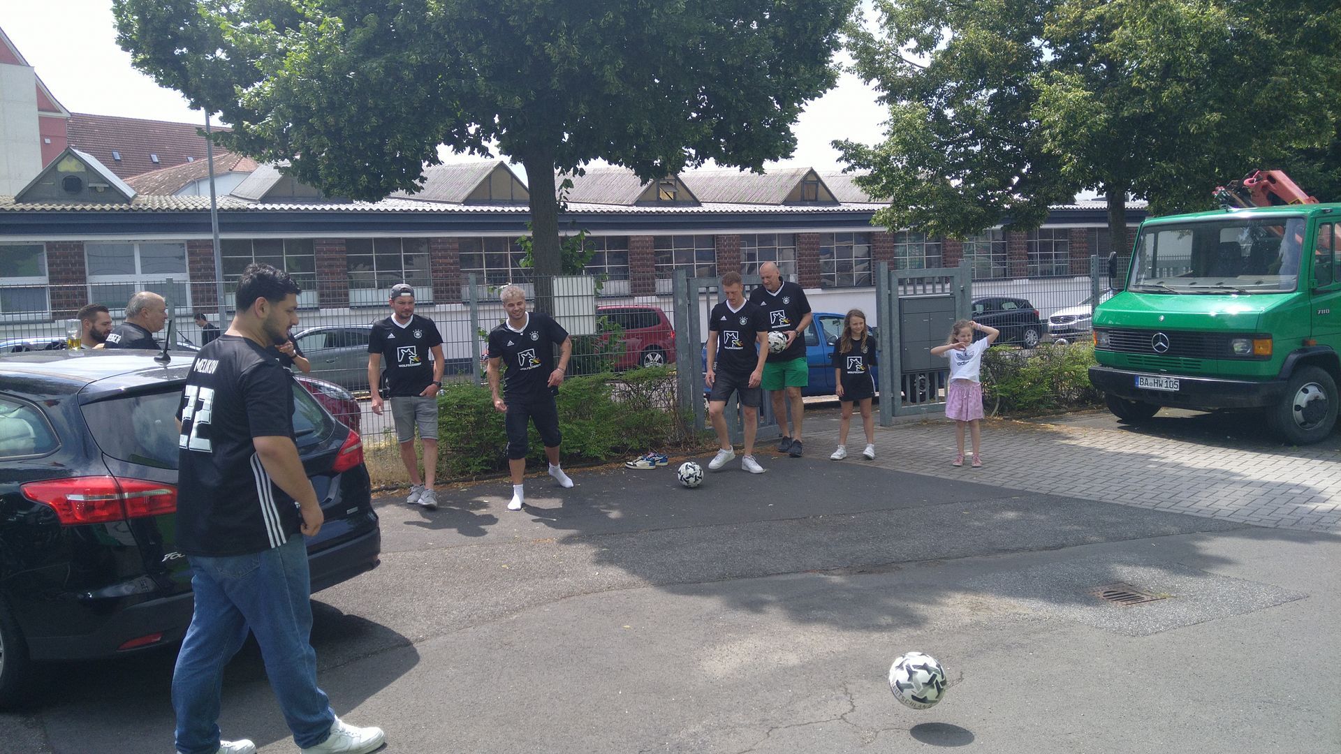 Eine Gruppe von Menschen steht auf einem Parkplatz um einen Fußball herum.