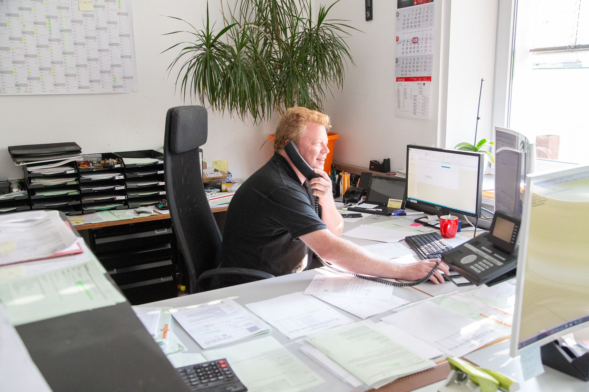 Ein Mann sitzt an einem Schreibtisch und telefoniert mit einem Mobiltelefon.