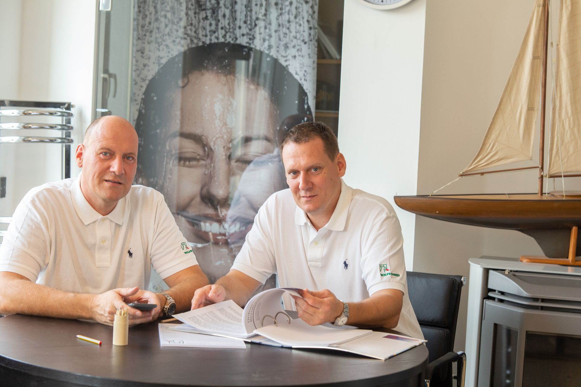 Zwei Männer sitzen an einem Tisch und schauen sich ein Buch an.