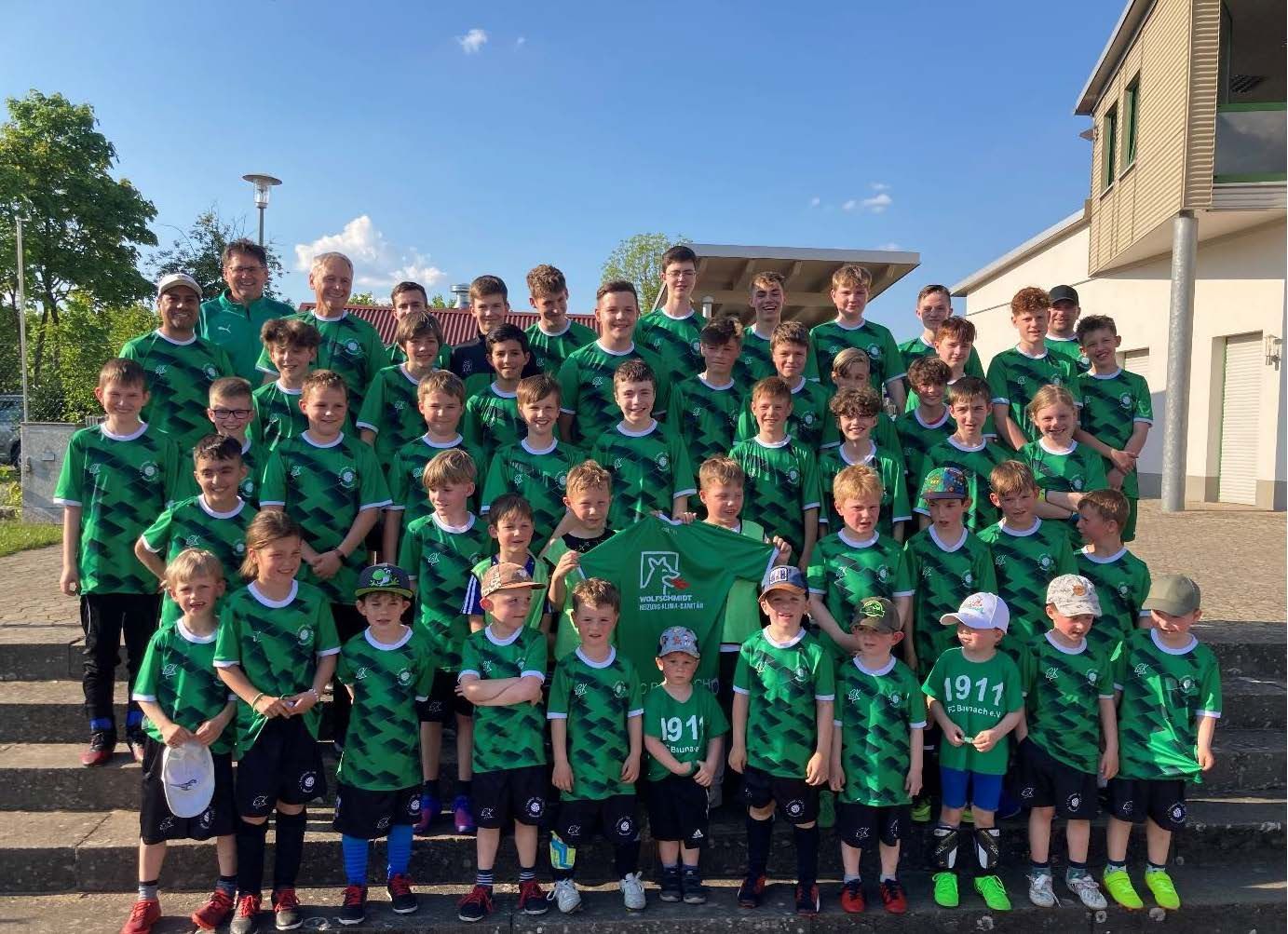 Eine große Gruppe von Kindern in grünen Hemden posiert für ein Foto.