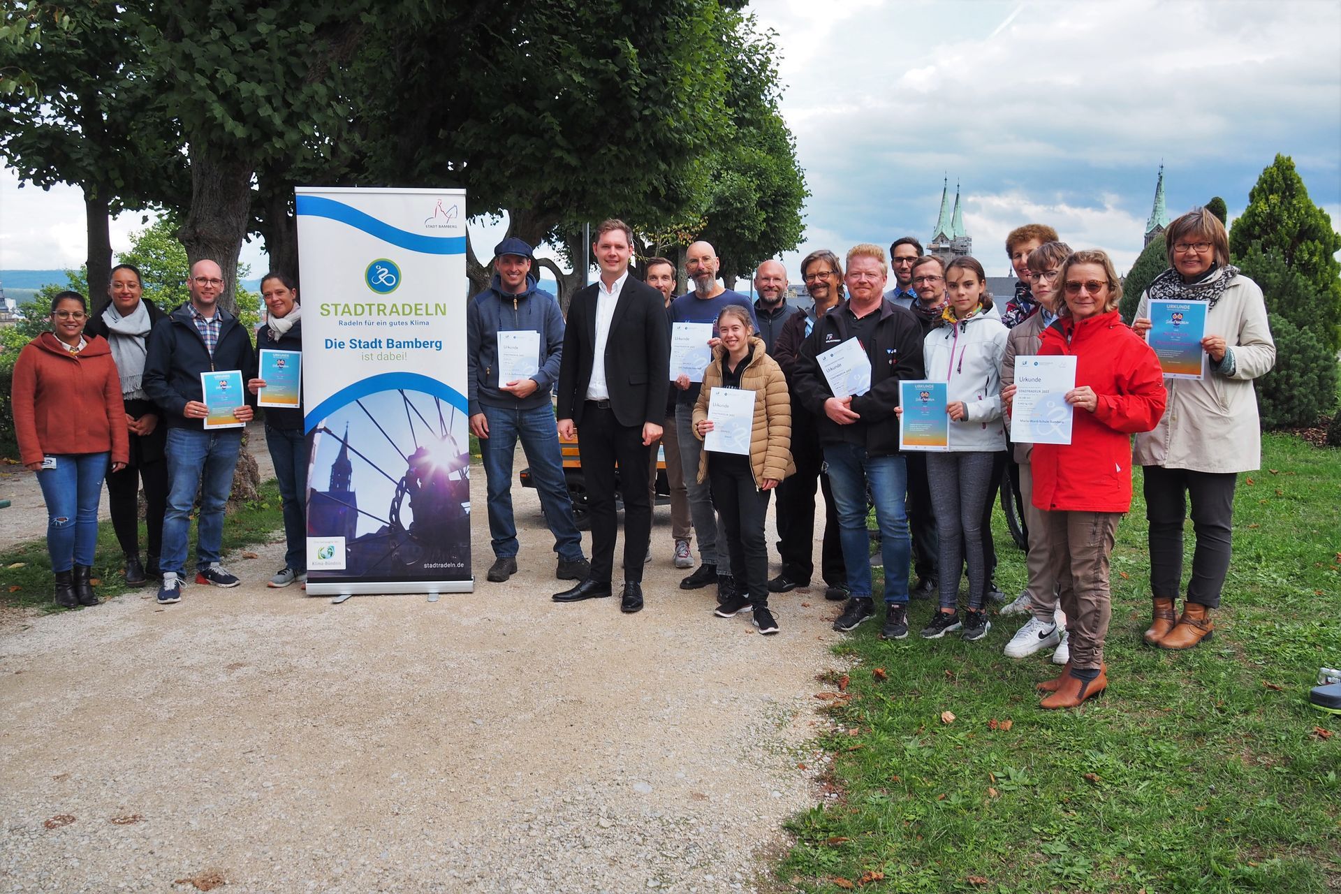 Eine Gruppe von Menschen steht vor einem Schild und hält Zertifikate in den Händen.