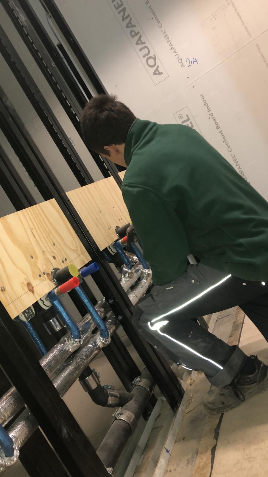 Ein Mann in einer grünen Jacke steht in einem Raum mit Rohren.