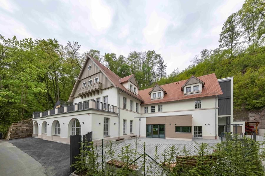 Ein großes weißes Haus mit rotem Dach ist von Bäumen umgeben.