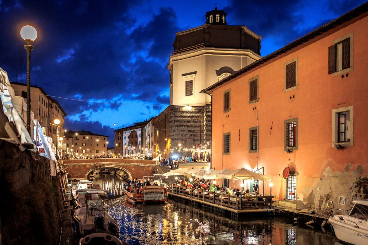A boat is docked in front of a building next to a river at night.