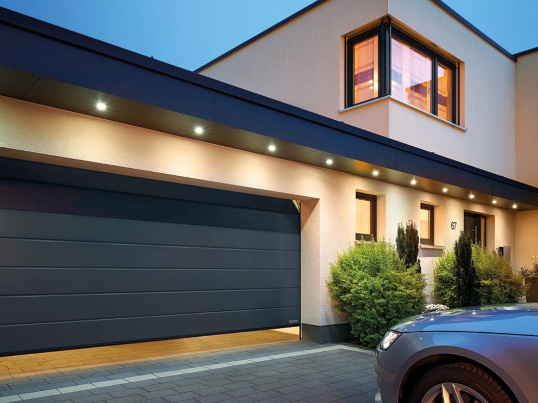 Una puerta de garaje negra está abierta delante de una casa.