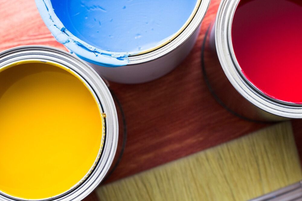 Tres latas de pintura y un pincel sobre una mesa de madera.