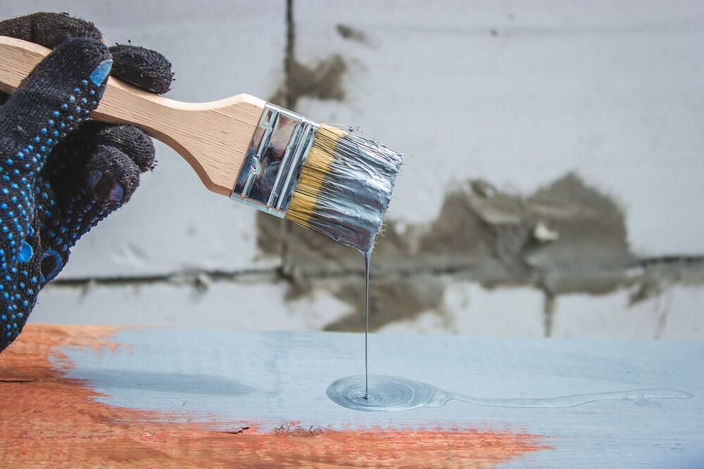 Una persona sostiene un pincel y vierte pintura sobre un trozo de madera.