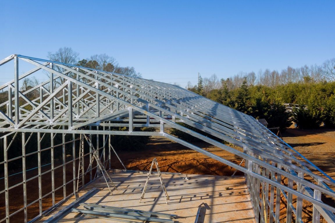 Metallrahmen eines im Bau befindlichen Gebäudes, mit blauem Himmel und Bäumen im Hintergrund.