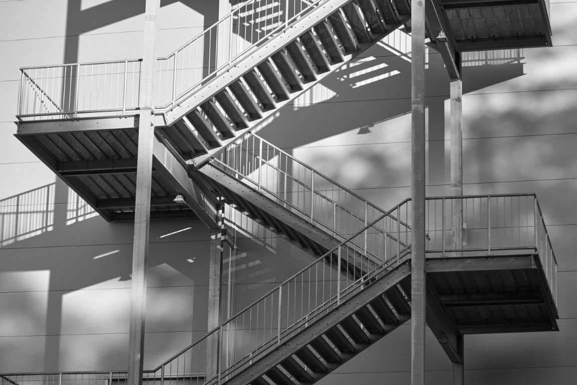 Schwarz-weiße Feuertreppe aus Metall an einer Gebäudewand mit Schatten.