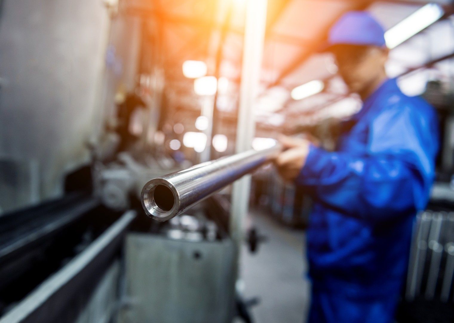 Person im blauen Overall schleift Metall, Funken fliegen, Industrieumgebung.