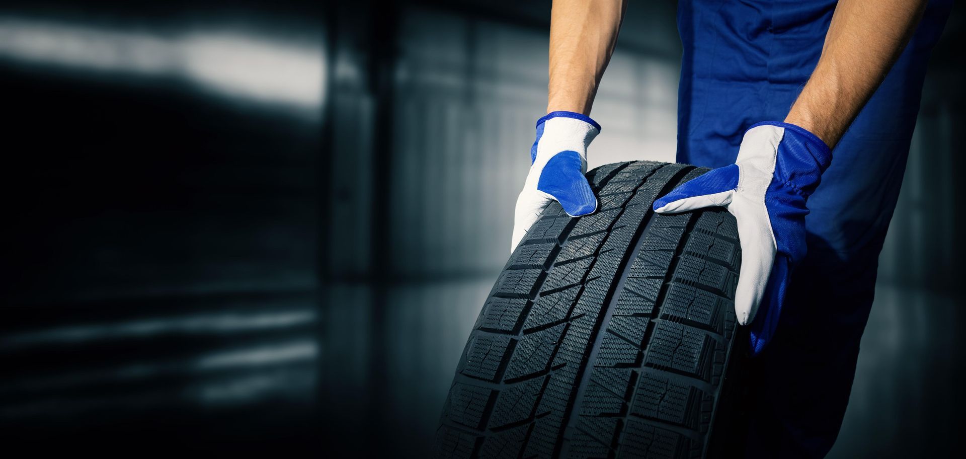 Person mit Handschuhen hält einen Reifen in einer dunklen Industrieumgebung.