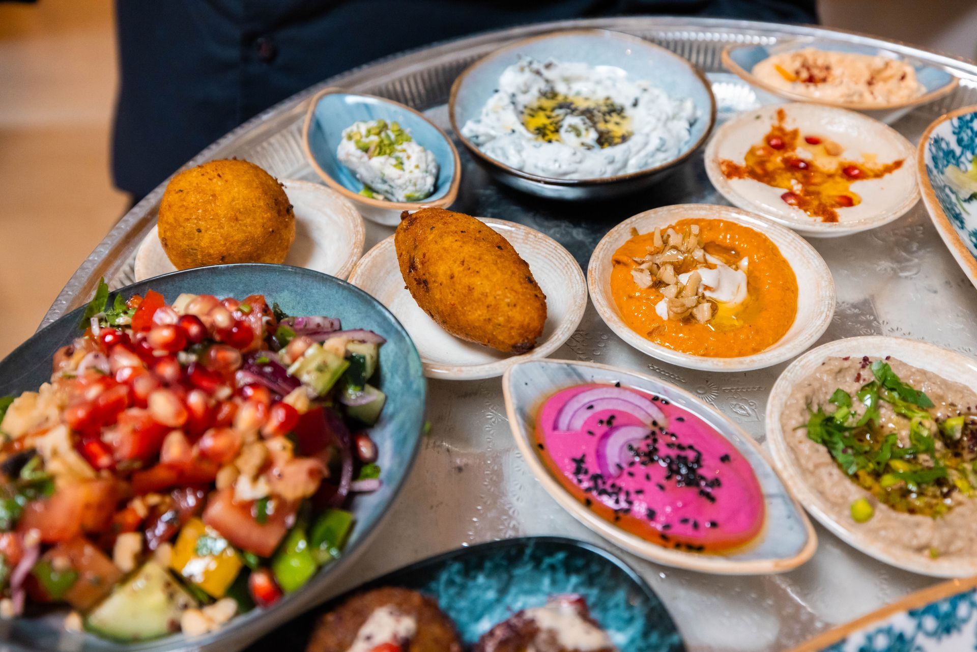 Innenansicht eines schwach beleuchteten Restaurants mit Bar, Hockern, Tischen und verschwommenen Gestalten von Personal und Gästen.