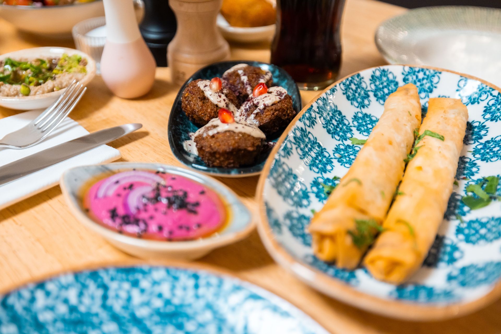 Menschen um einen Holztisch, die nach verschiedenen Tellern mit Essen greifen, Aufnahme von oben.