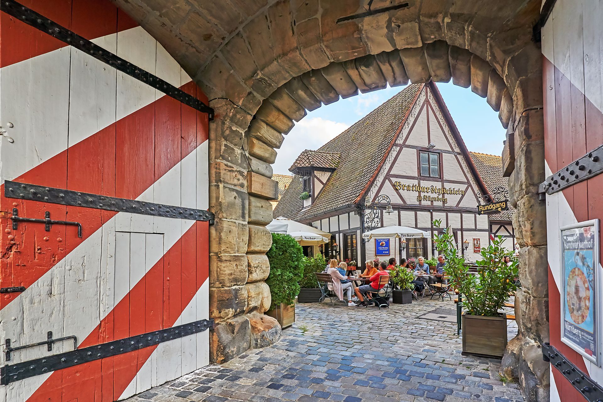Ein gemauerter Torbogen, der zu einem Restaurant führt, vor dem Leute sitzen